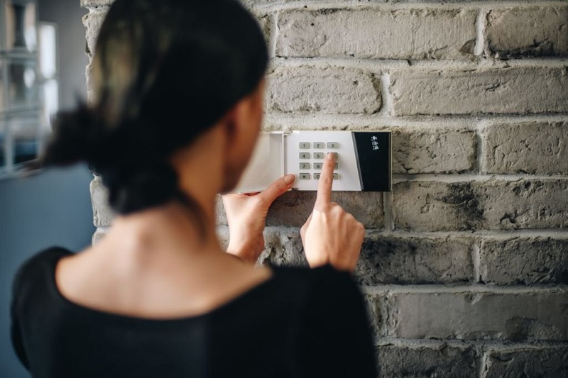 Young woman entering security pin on home alarm keypad. Home security system